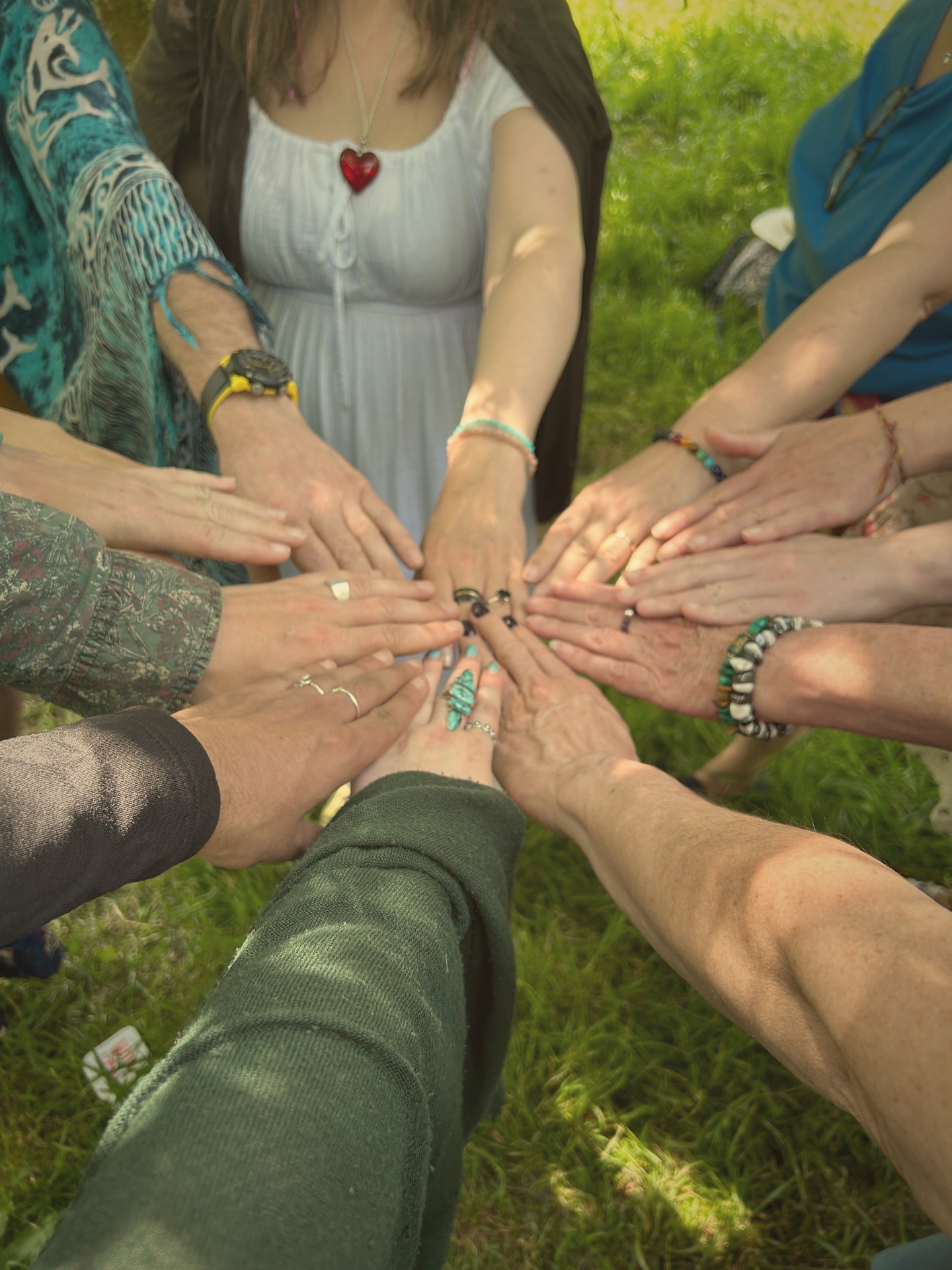 A circle of hands joined together over the grass on a sunny day